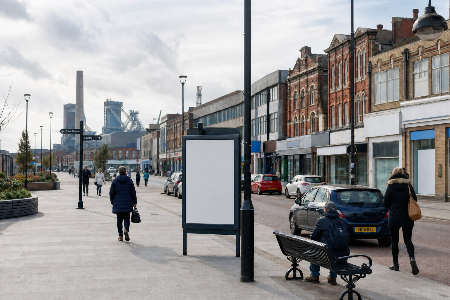 A quiet urban street scene with people walking, industrial buildings in the background, and a blank advertising board in the foreground.