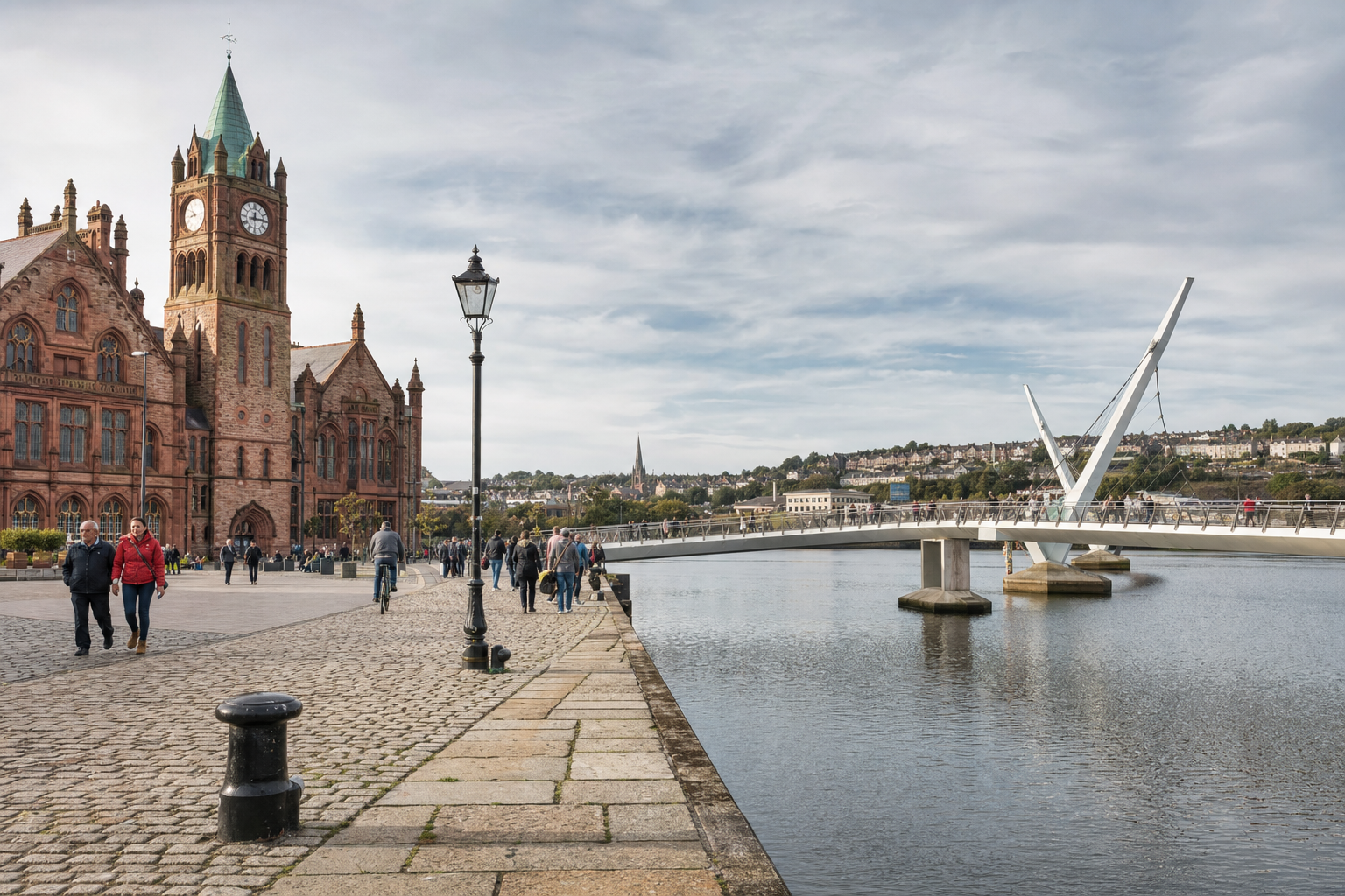 People walking near a historic clock tower and modern bridge by a riverside on a clear day.