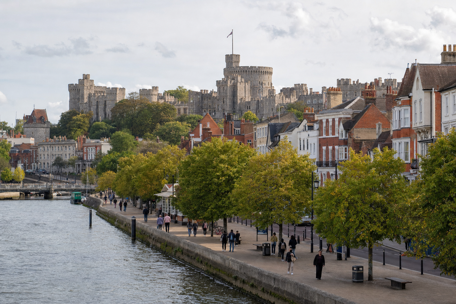 Windsor Castle towers above a riverside promenade lined with trees and historic buildings.