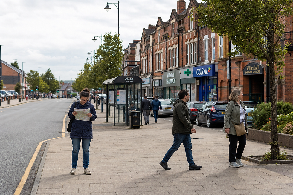 A woman reads a map on a street in Willenhall, with shops and pedestrians in the background.