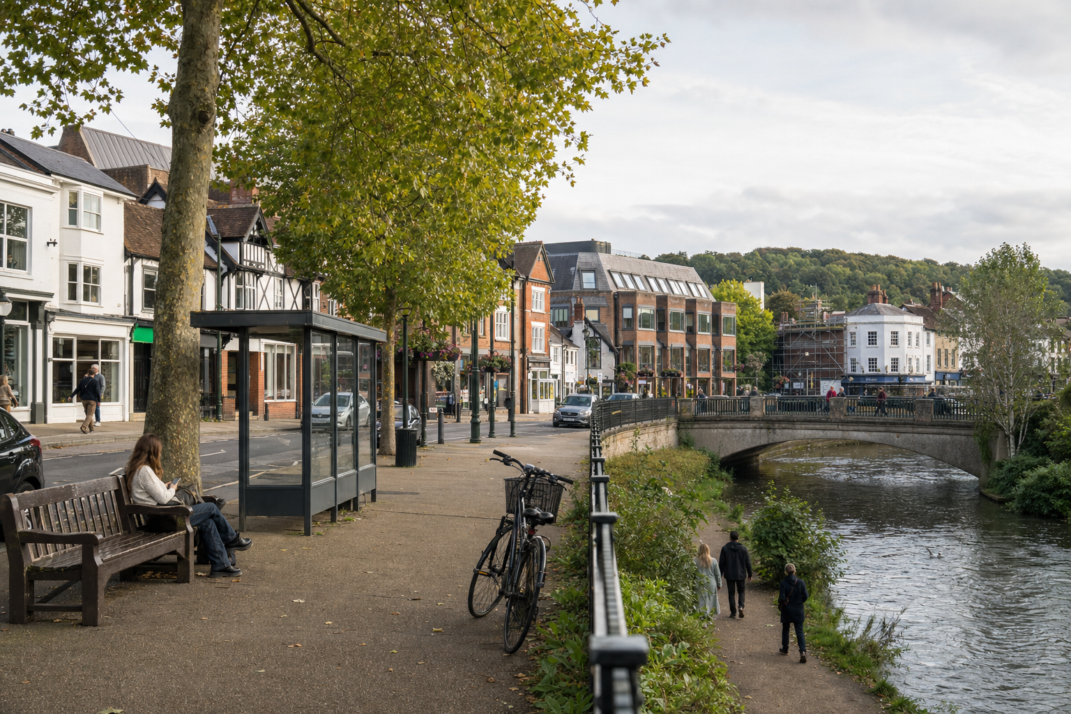 A riverside street with a bench, bicycle, and people walking near historic buildings.