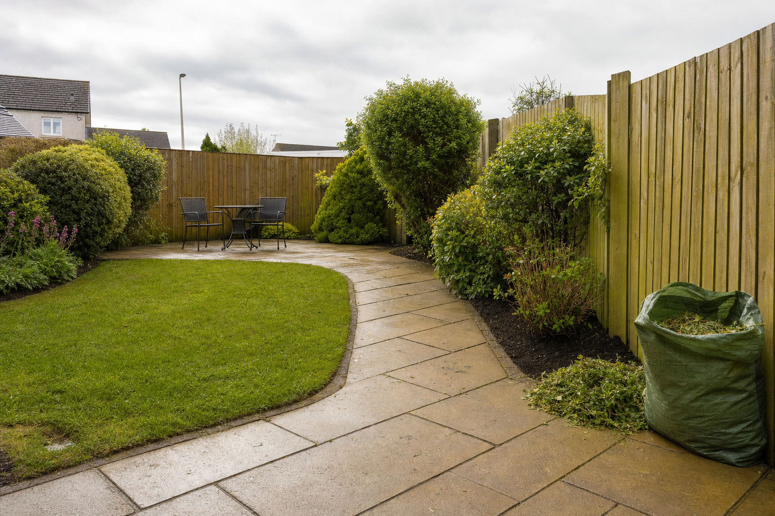 A neatly landscaped garden with a patio path, outdoor seating, and a bag of garden waste near a wooden fence.