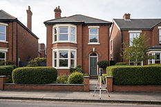 Red brick detached house with bay windows and a camera on a tripod in the foreground.