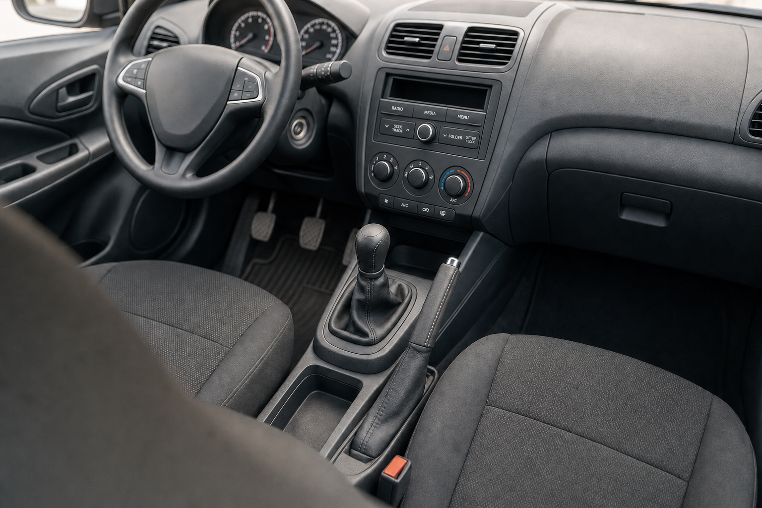 Interior view of a car showing the steering wheel, gear stick, and control panel with manual transmission.