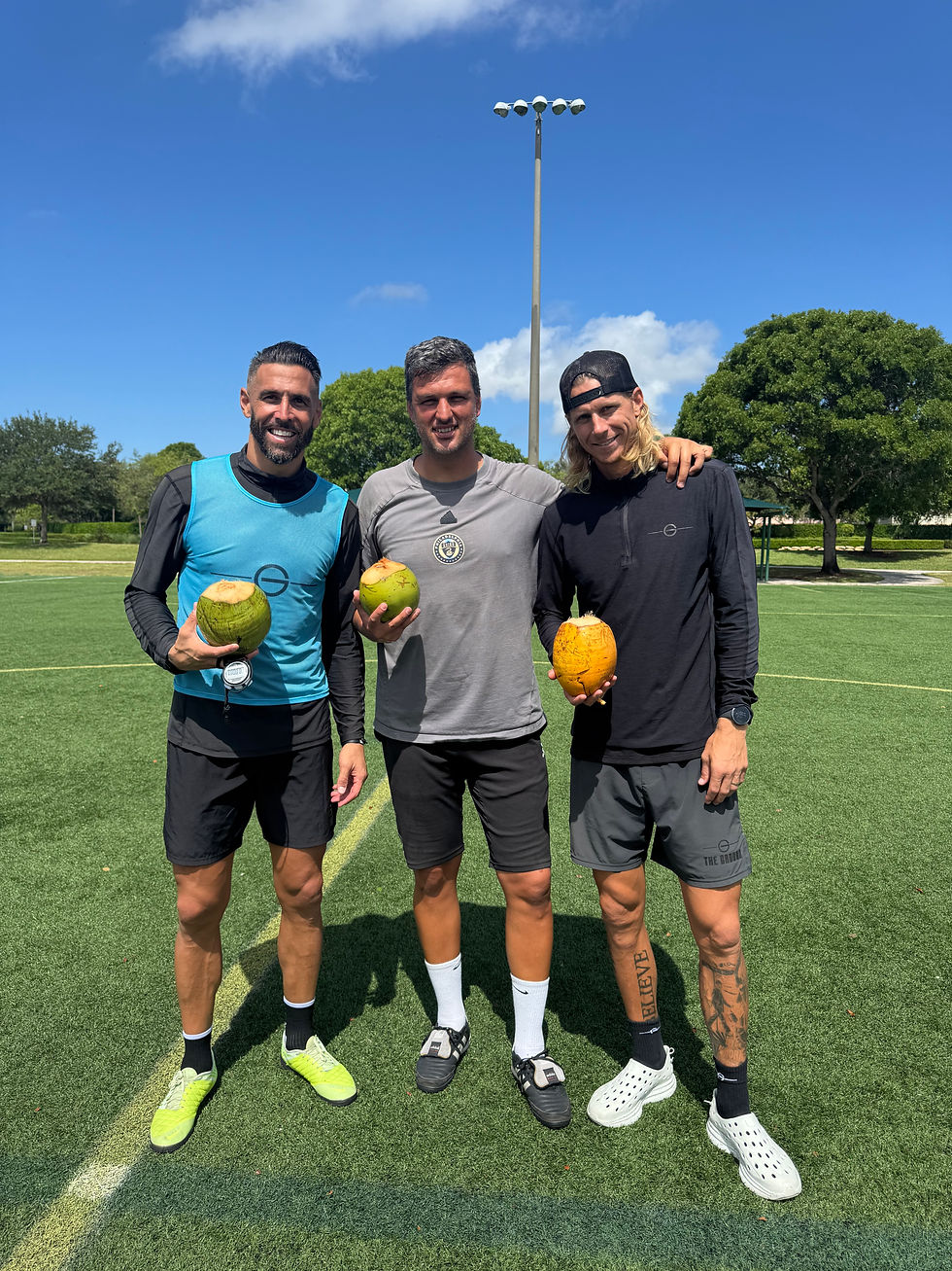 Three adult soccer coaches holding coconuts and smiling on the soccer field