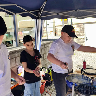 Kinder und Jugendliche backen gemeinsam Waffeln an einem AWO Stand unter einem Pavillon