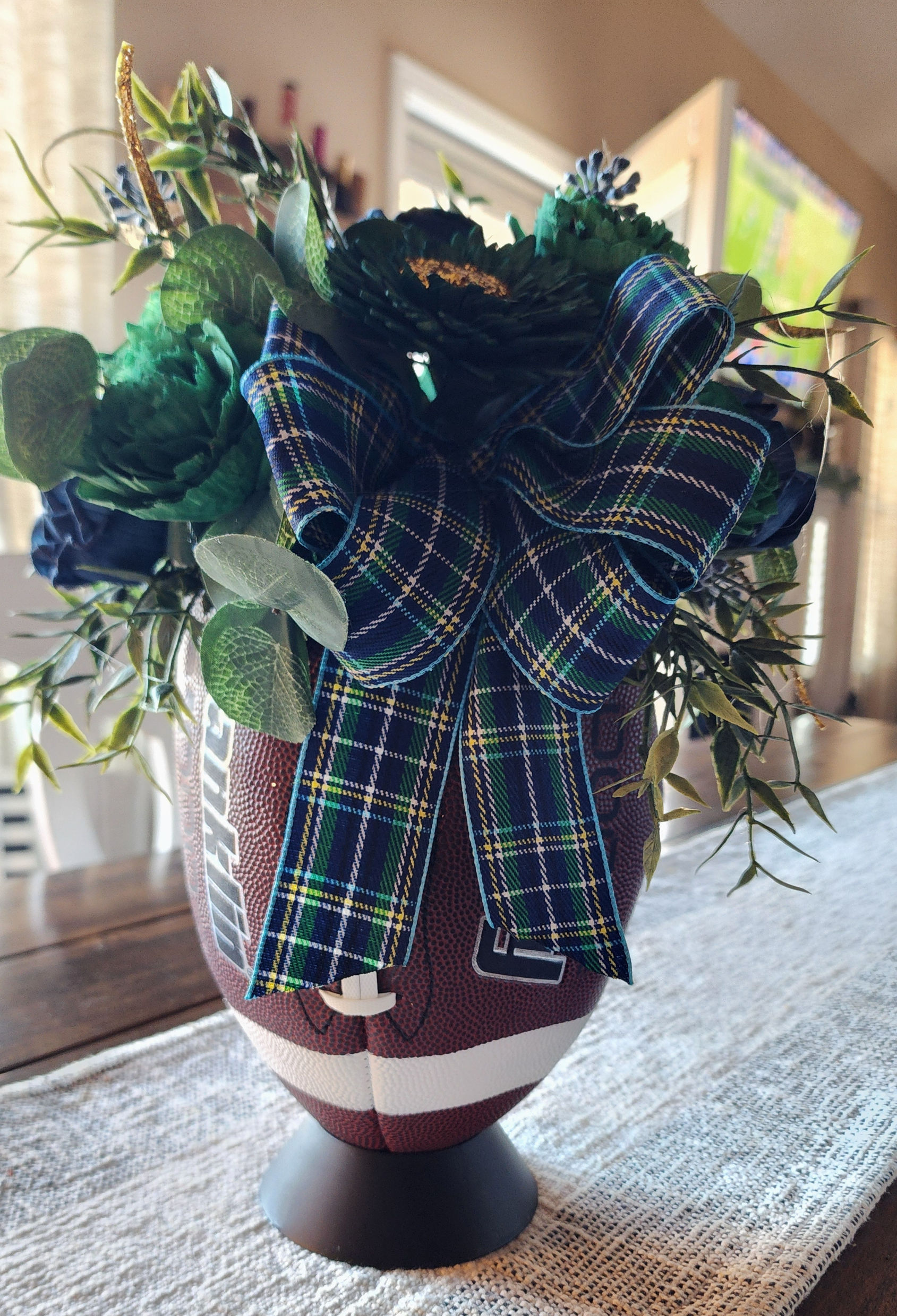 Custom sola wood football floral arrangement in team colors, featuring a football-shaped container and greenery accents.
