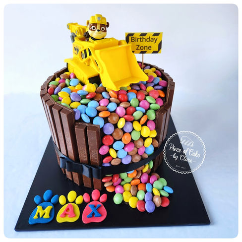 Construction themed chocolate cake with chocolate bar sides, colourful sweets spilling out and a yellow digger topper