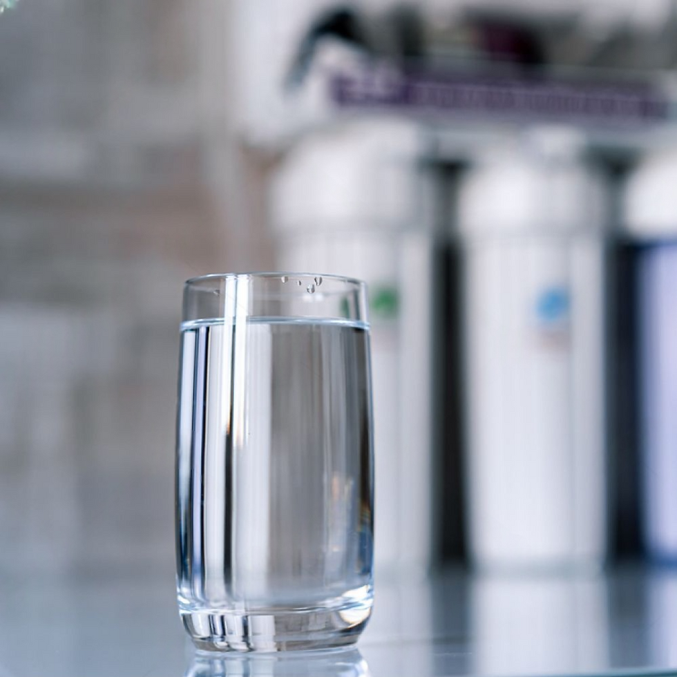 A clear glass of water on a reflective surface with blurred cylindrical objects in the gray background, creating a serene mood.