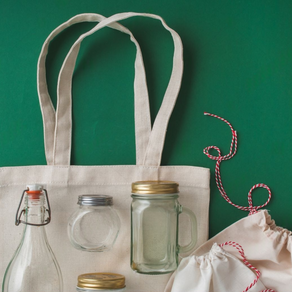 Reusable shopping bag, glass jars, bottle, and drawstring pouch on green background. Red and white string adds a festive touch.