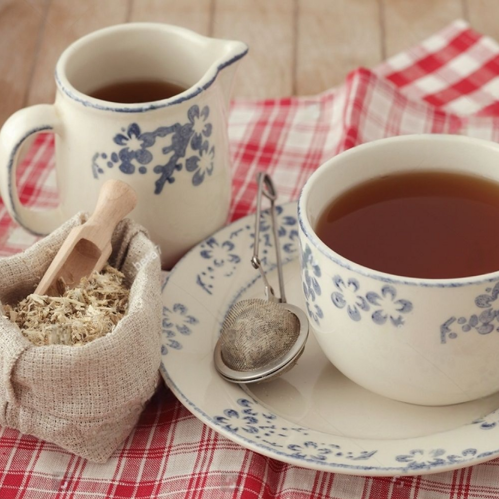 Floral teacup and pitcher on red checkered cloth with a herbal tea bag and infuser. Rustic, cozy setting.
