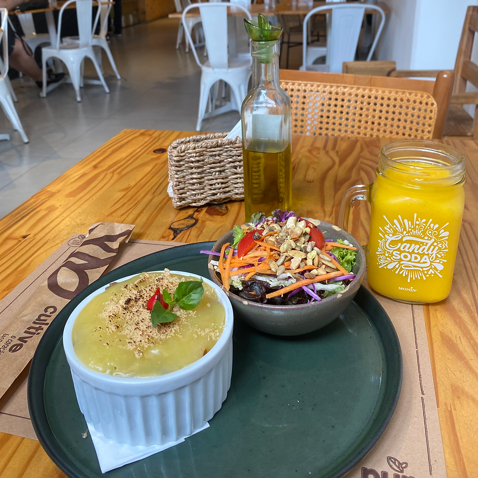 Salad and yellow pudding on a wooden table with olive oil bottle and orange drink in a jar labeled "Candy Soda" in a cozy café.