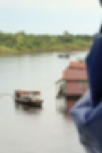 Boats on a calm river beside a pink house with a corrugated roof. Green forest in the background.