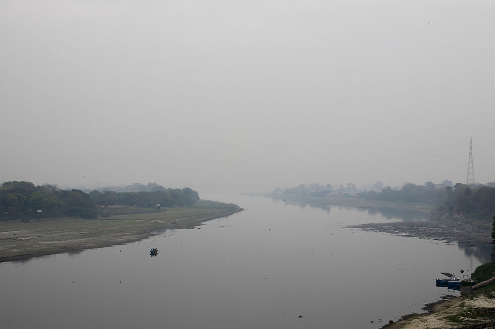 A small boat on a calm river, surrounded by greenery and misty, overcast skies. A power line tower is visible in the background.