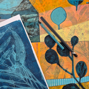 Art supplies on colorful abstract prints: blue leaf image, pencils crossed on orange-yellow paper, calm creative workspace
