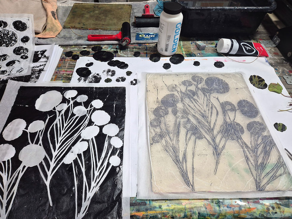 Printmaking workspace with botanical monotype proofs, brayers, ink, and a GOLDEN bottle on a paint-splattered table.