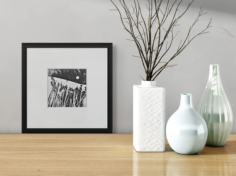 Framed abstract art on a wall beside white and pale blue vases with branches. Wooden surface, minimalistic and calm setting.