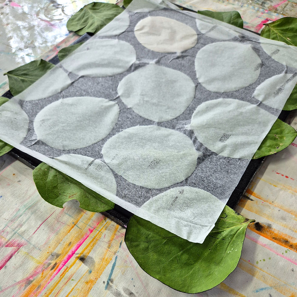 Paper with gray circles on a canvas, surrounded by green leaves. Background has colorful paint streaks. Creative and artistic setting.