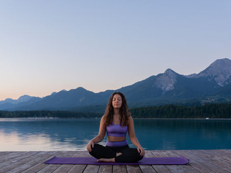 Nő meditál egy tóparton, hegyekkel a háttérben