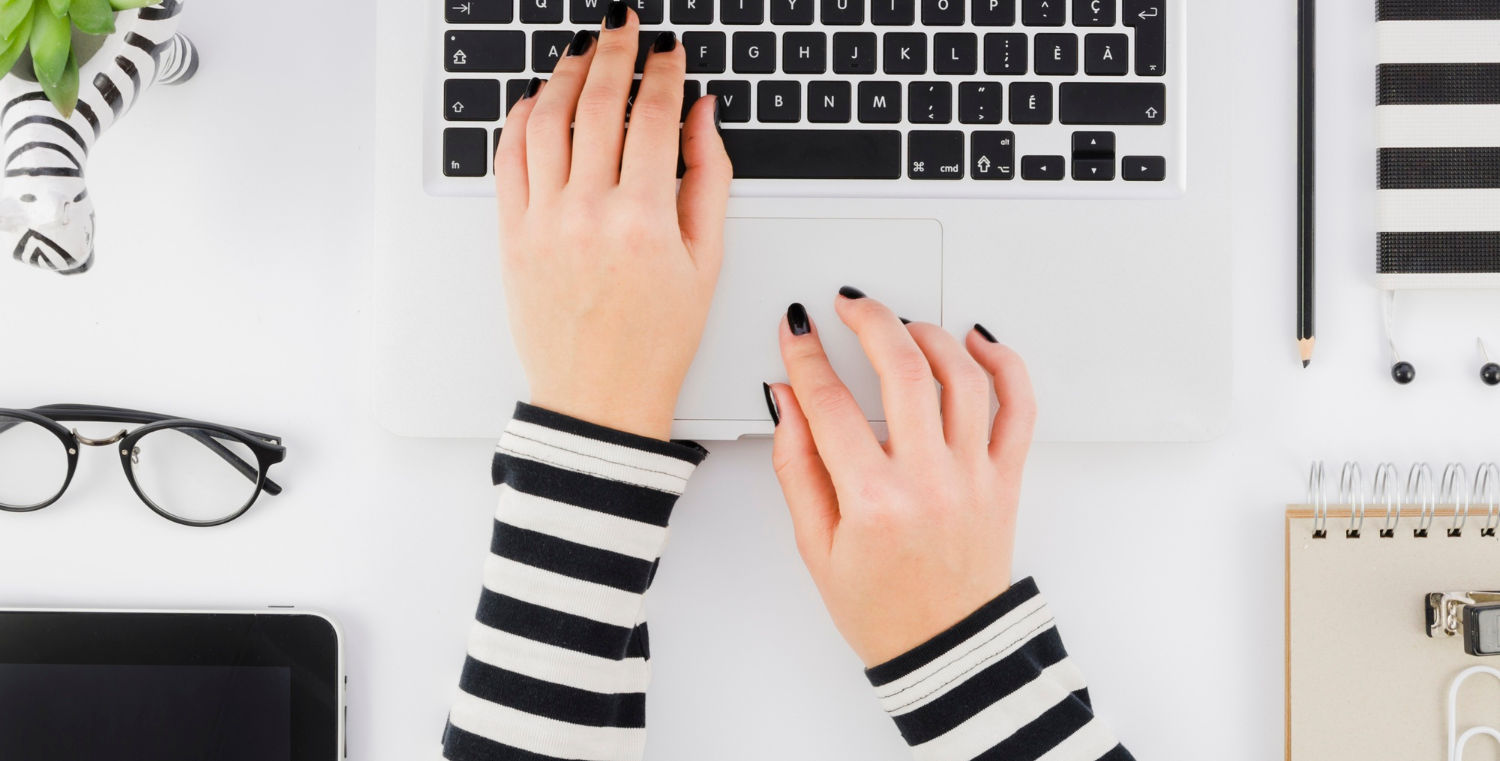 Image d'un bureau et des mains de femme qui tapent sur le clavier d'un ordinateur portable.