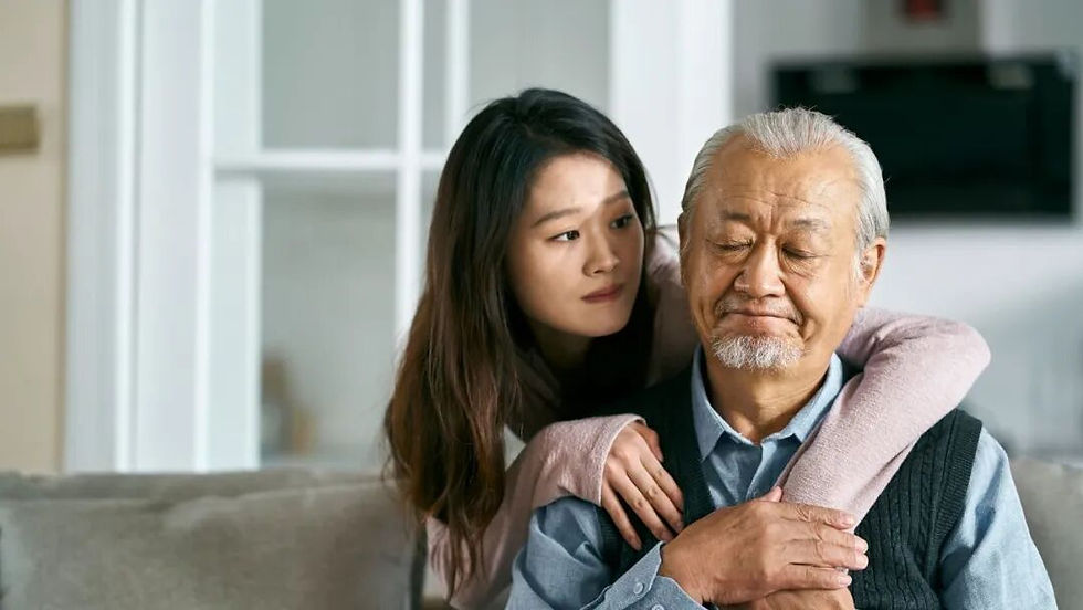 女兒在客廳裡從背後摟著閉眼的父親,兩人坐在沙發上,神情安靜溫柔,背景為明亮室內。
