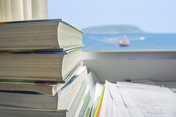 窗邊有幾本厚厚的書和紙張,背景是藍色的海景,一隻小船在遠處清晰可見,陽光明媚,氛圍寧靜。