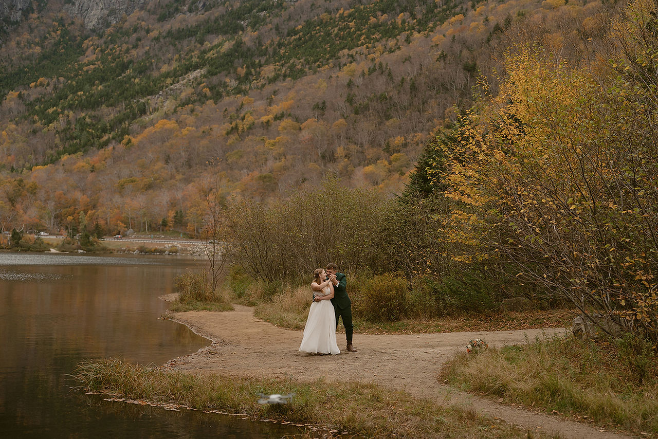 Couple exploring lake side in moody weather on a fall day in the white mountains after micro wedding