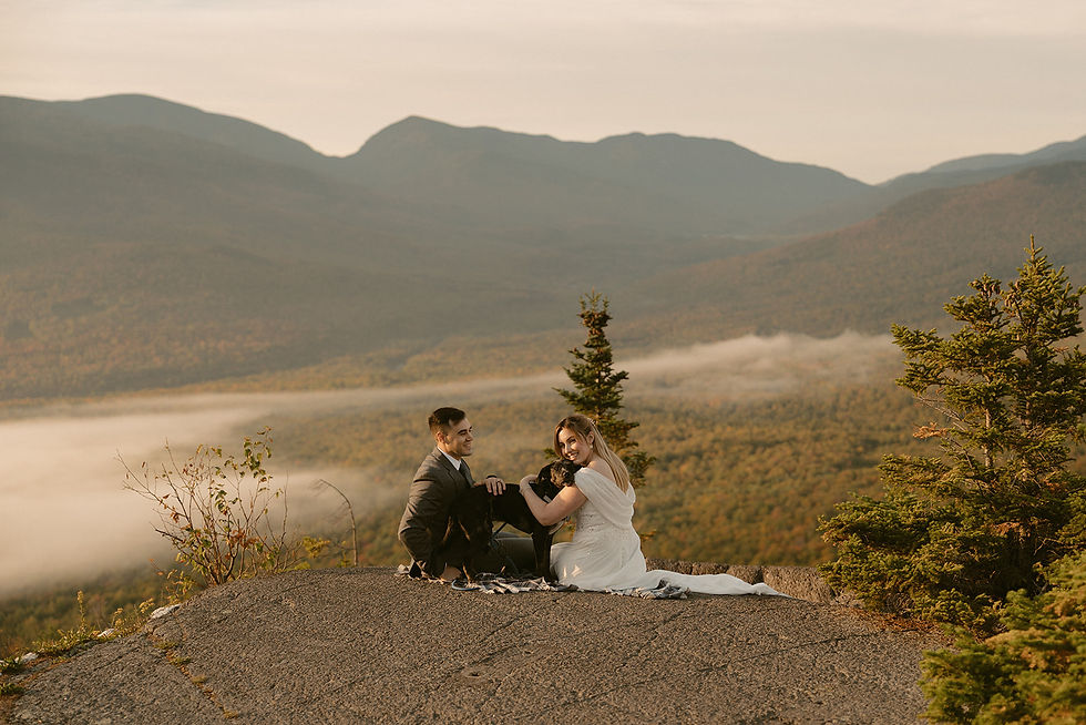 Couple sitting down on mountain top enjoying view and cuddling with dog on elopement day