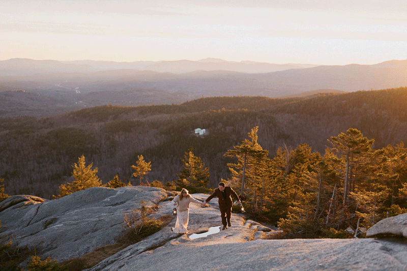 GIF of couple walking up a mountain in the mountains with lanterns as the sunsets on wedding day