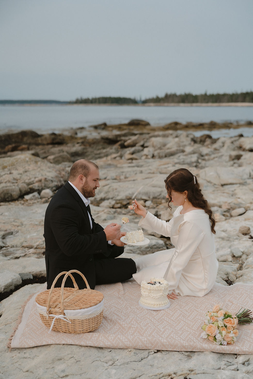 couple on elopement day at seawall picnic area enjoying a picnic and first bites of cake in acadia