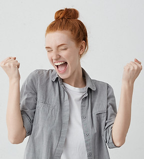 Caucasian freckled woman with red hair rejoicing her success and victory clenching her fis