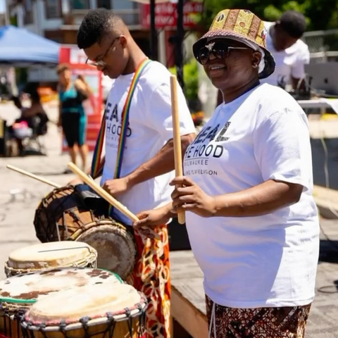 Chapter founder Oju drumming at a sunny outdoor event with Drums Up Guns Down participant to her right