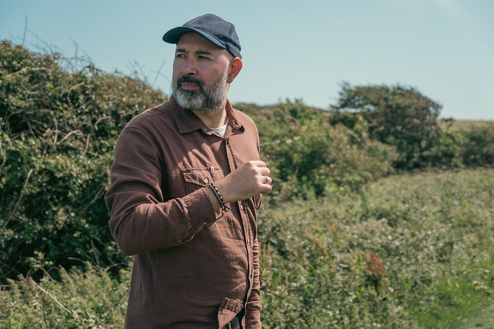Bearded man in a brown overshirt and cap outdoors, wearing a handmade men's silver bracelet on his wrist