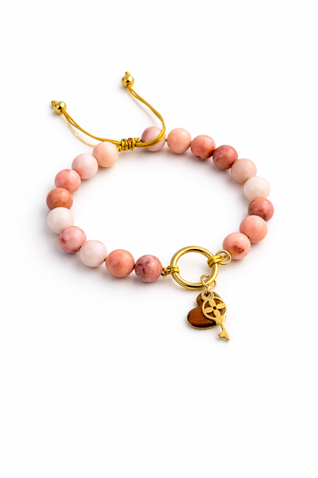 Pulsera artesanal Iria con cuentas de aventurina rosa en tonos suaves y dijes dorados de corazón y llave. Cierre ajustable.