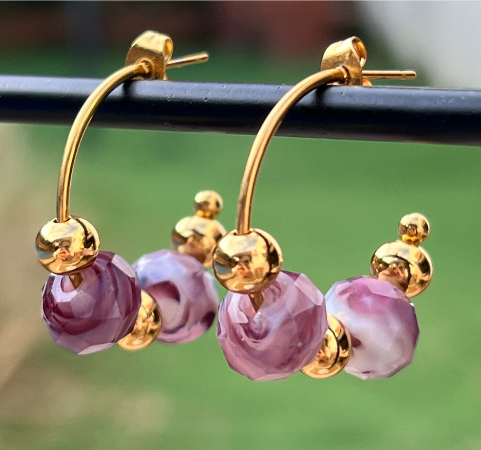 Pendientes Murata hechos a mano con cristal de Murano en tonos malva y rosa veteado, montados sobre una estructura de acero hipoalergénico dorado. Su diseño curvado y elegante combina sofisticación y modernidad, ideal para realzar cualquier look con un toque exclusivo y artesanal.