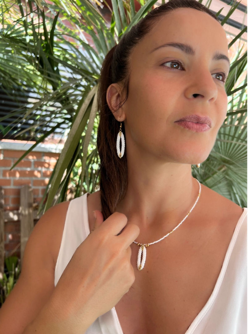 Miniatura: Modelo con expresión serena luciendo el colgante y pendientes Lía blancos en un entorno natural, exclusivo de Pulserea