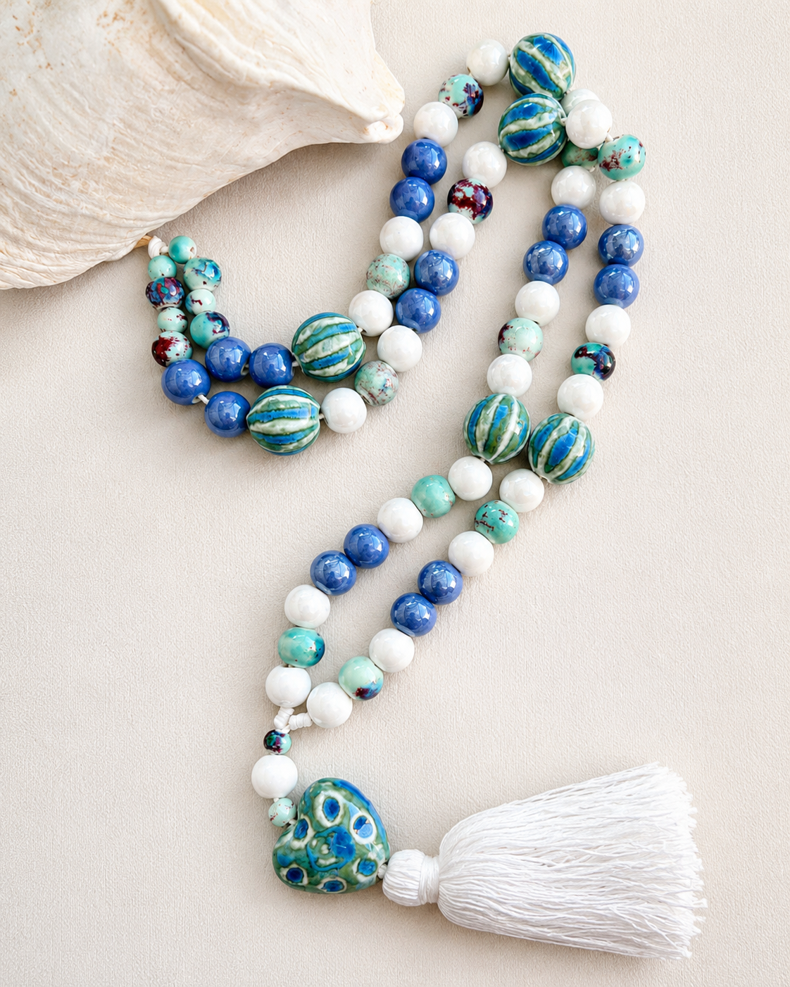 Detalle de collar artesanal Mika de cerámica con dije de corazón azul y borla blanca.