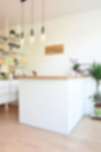 The front desk of the Sanctuary, whichhas white walls and a light brown wooden countertop, decorated with flowers and plants