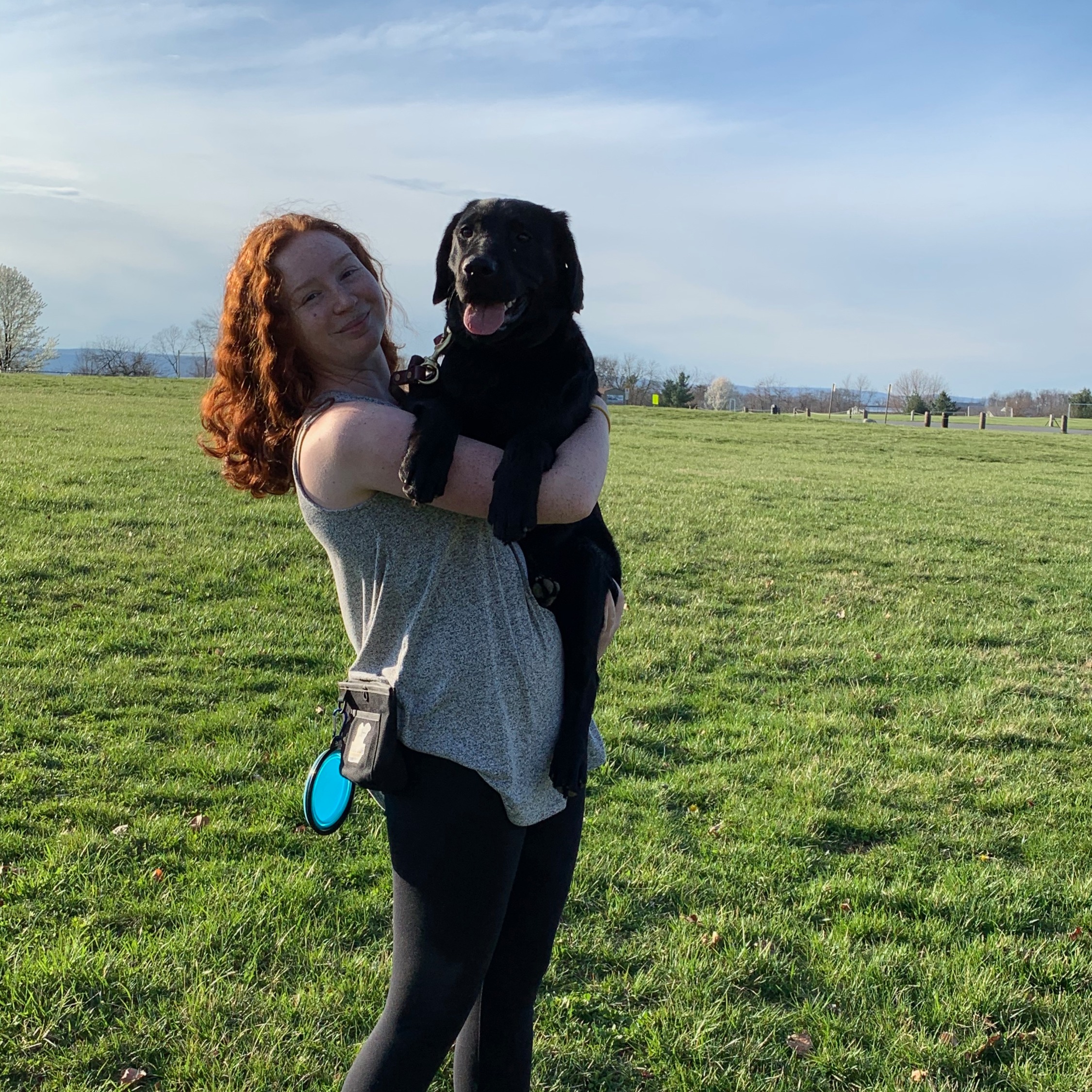 Kaitlyn stands in a grassy field and holds a black lab.