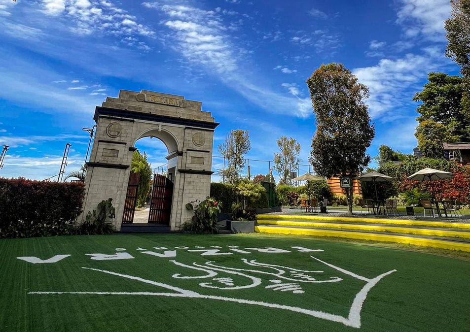 Trizara-branded green lawn beside an ornamental arch and trees.