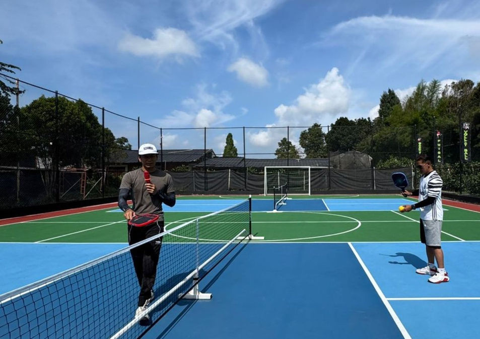 Two people playing a racket sport on a blue and green outdoor court at Trizara.