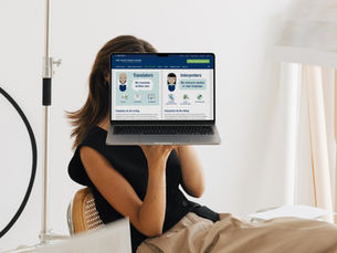 Woman sitting in a minimalist workspace holding a laptop in front of her face, displaying a blog post from the American Translators Association (ATA) explaining the difference between translators and interpreters