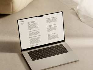 Un MacBook mostrando el sitio web de una traductora profesional está colocado en un suelo de color claro en una habitación con iluminación suave. La pantalla presenta a Inés Bellesi como traductora e intérprete certificada por NAATI de inglés a español. Un otomano beige con textura y cortinas blancas fluidas aportan una estética minimalista y elegante al ambiente.