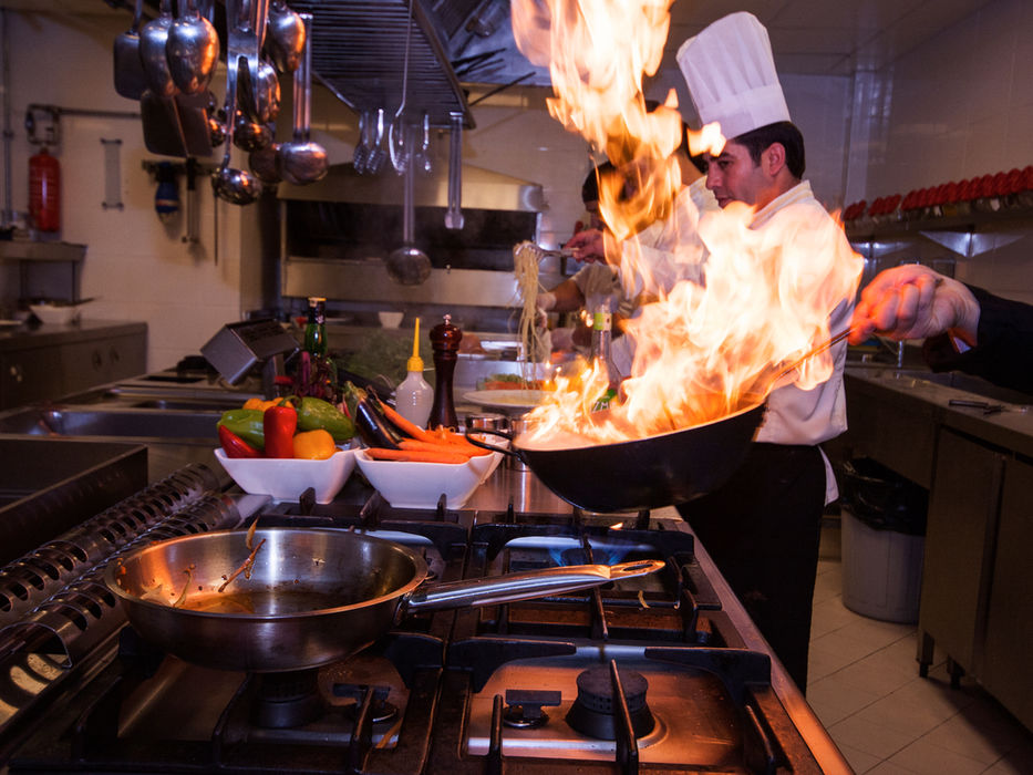Chef kocht Essen mit Flammen in einer Pfanne; Küche, Gemüse.