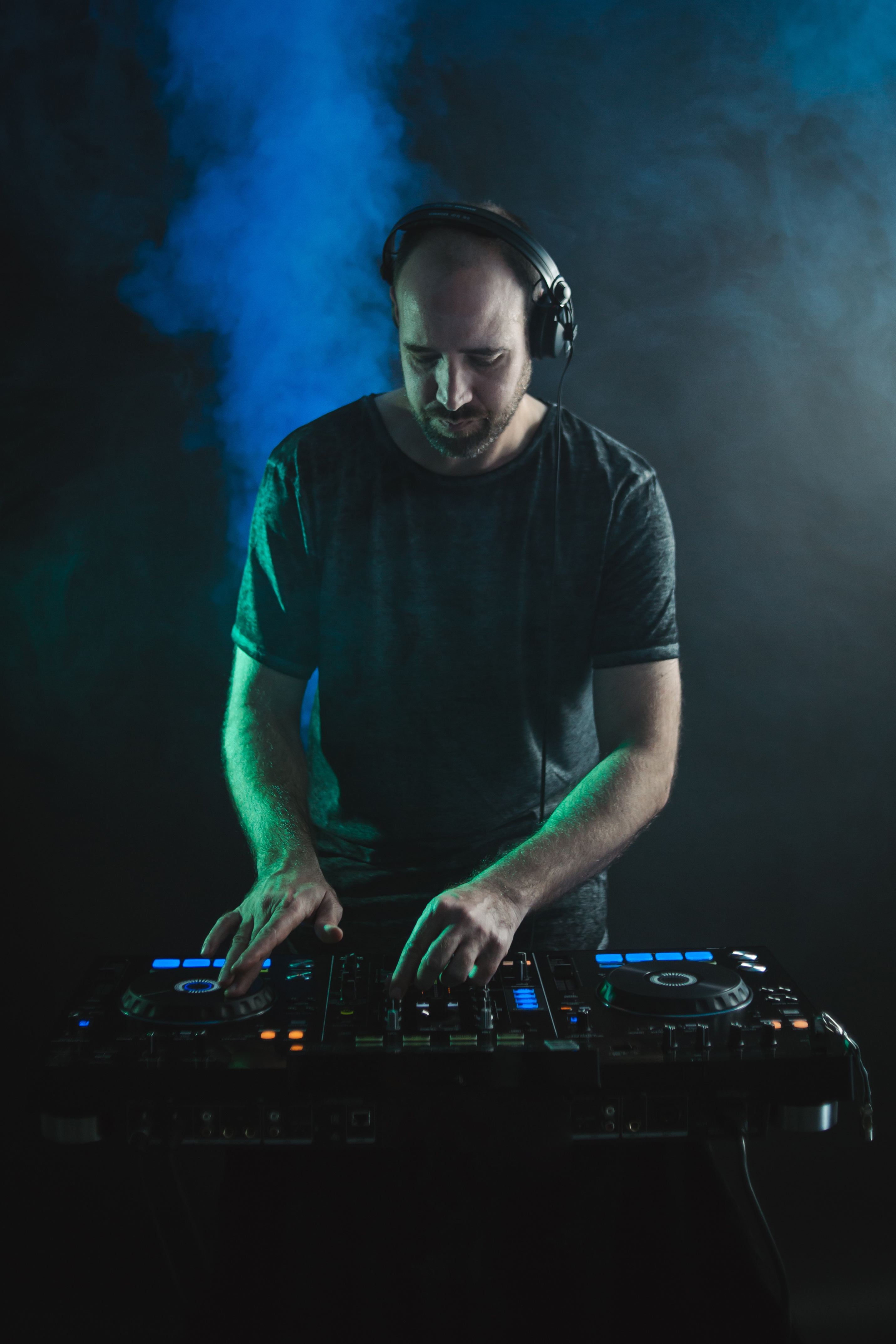 DJ spielt Musik an einem DJ-Pult, Hintergrund mit blauem Rauch. BeatsVibes