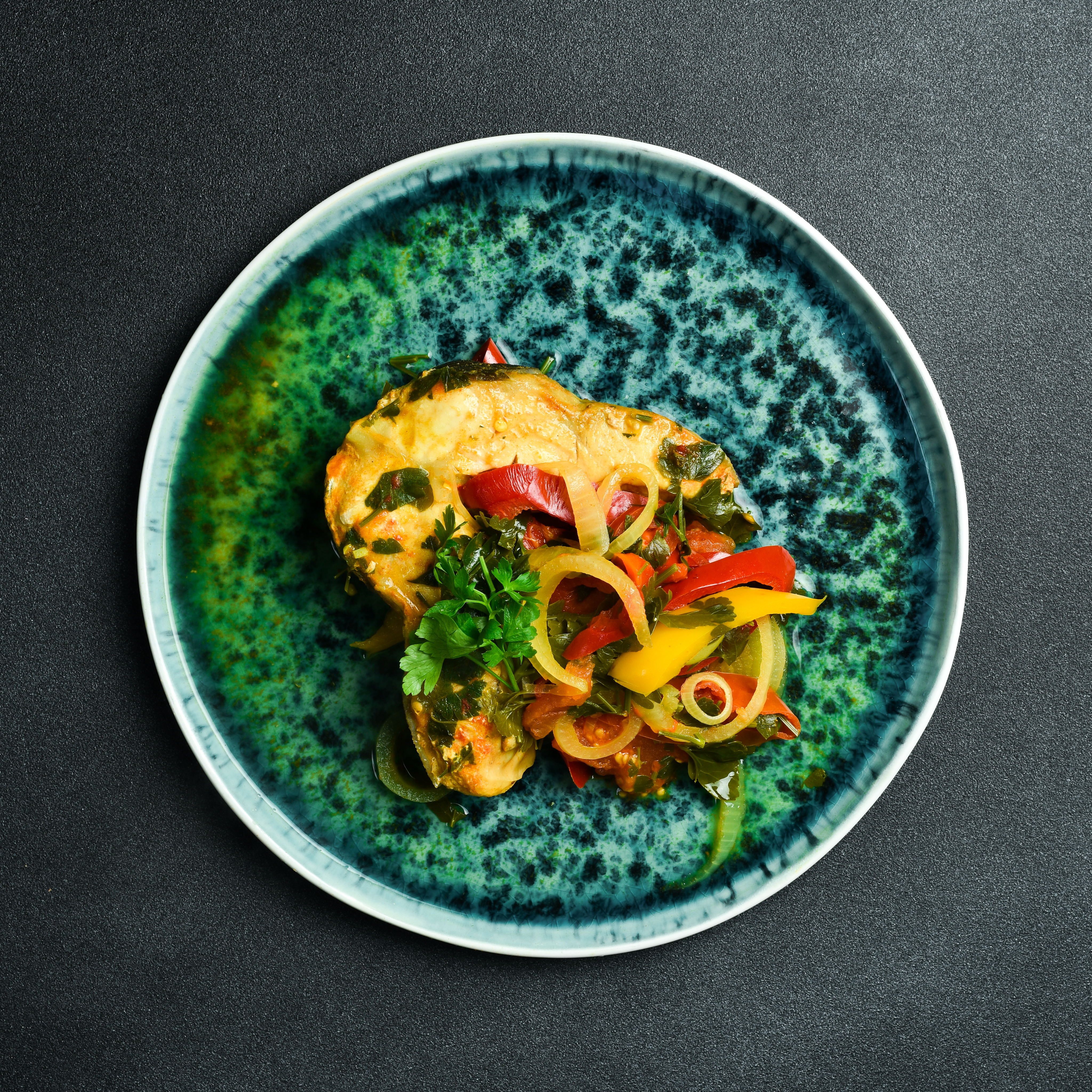 Gebratener Fisch mit Paprika und Kräutern auf grünem Teller