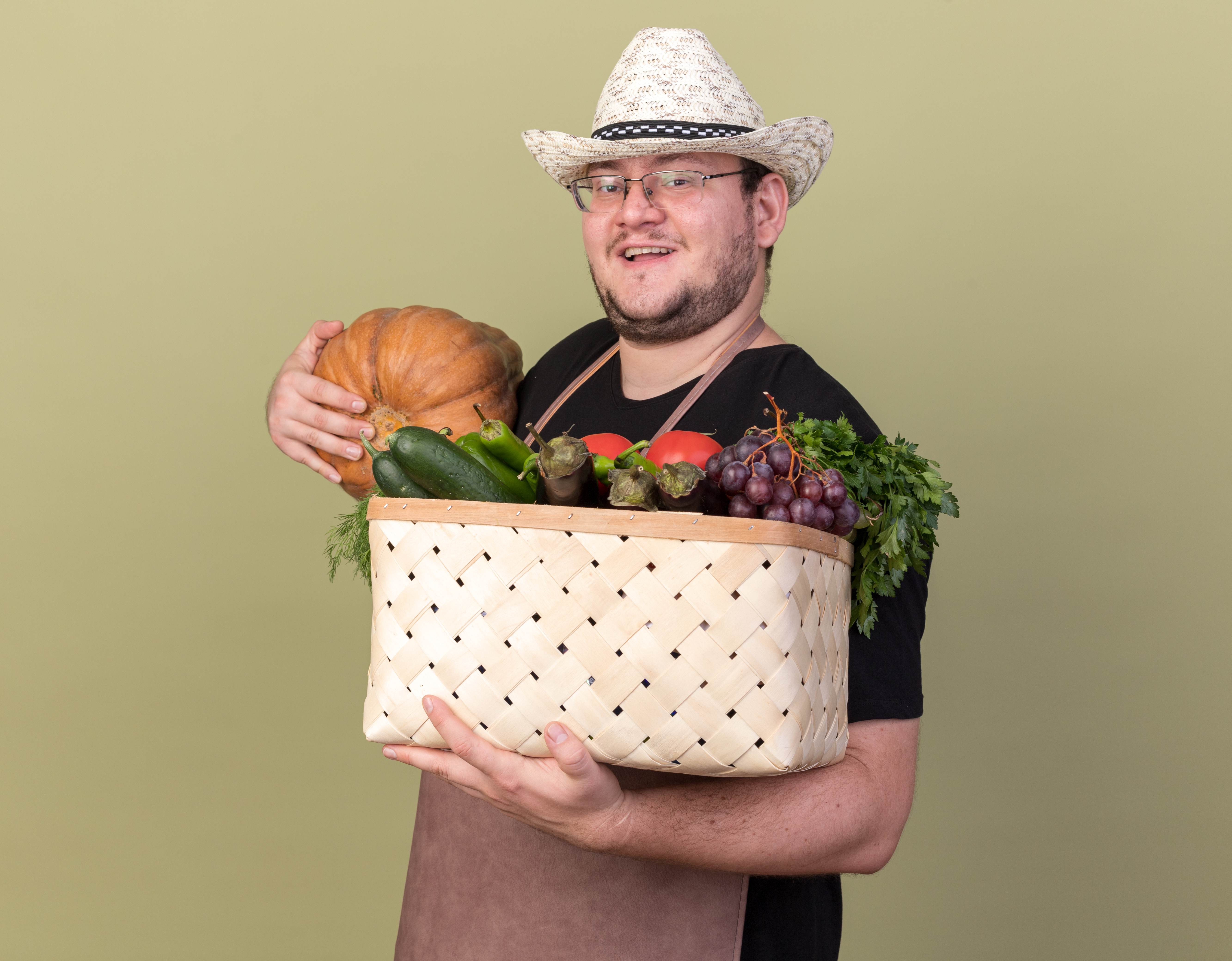 smiling-young-male-gardener-wearing-gardening-hat-holding-vegetable-basket-with-pumpkin-is