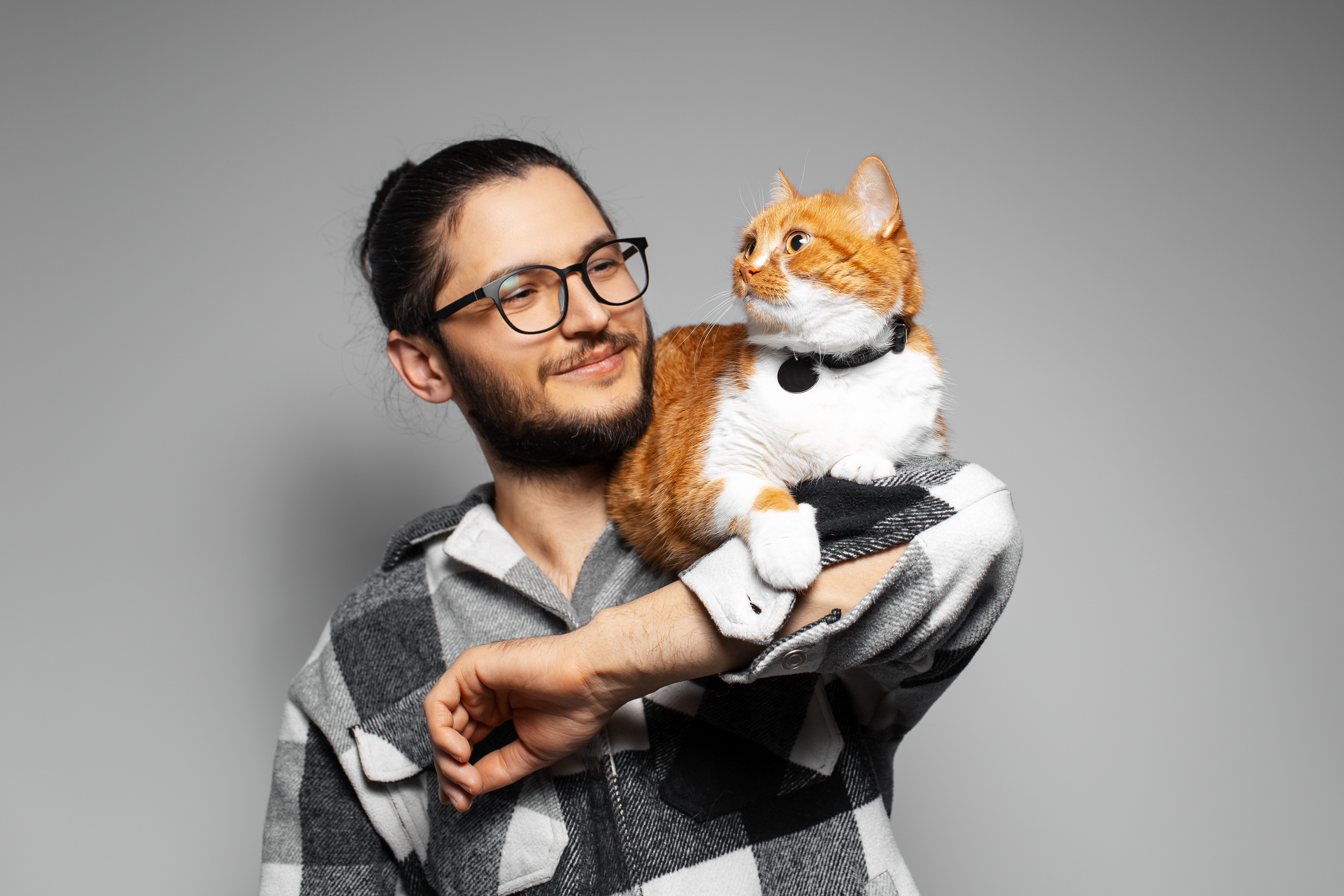 studio-portrait-young-smiling-man-with-red-cat-his-arms-grey-background.