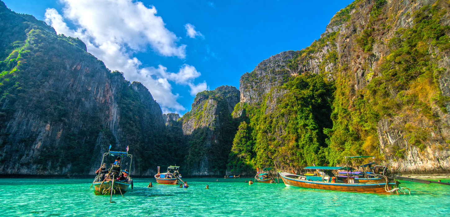 Boote fahren im türkisfarbenen Wasser, umgeben von grünen Bergen, TraumReisen.