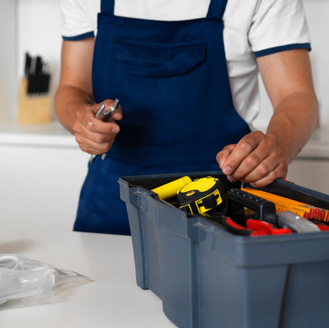 Handwerker in blauer Latzhose, Werkzeugkasten, bereit für Reparaturen in Küche.